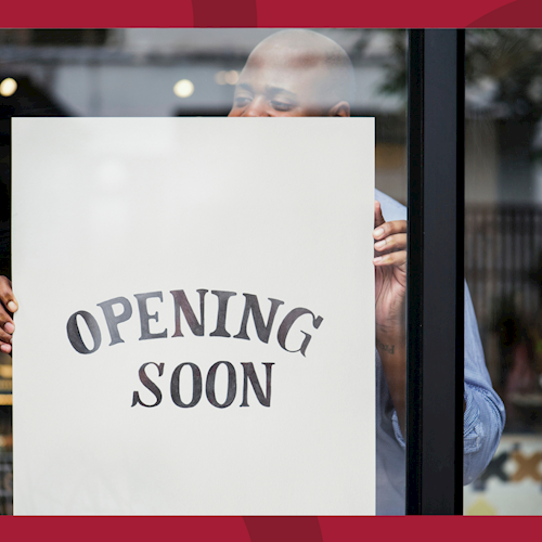 A man is putting an 'Opening Soon' sign in the window of a store.